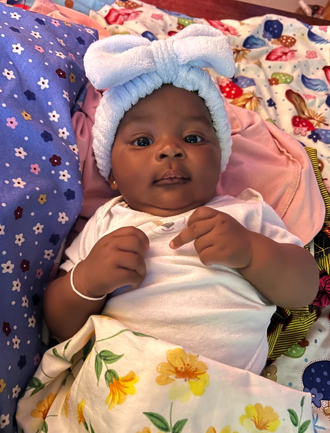 A Ghanaian newborn in a soft blue headband resting on a flowered blanket